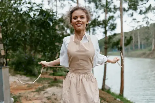 Улыбающаяся молодая женщина в бежевом фартуке у озера