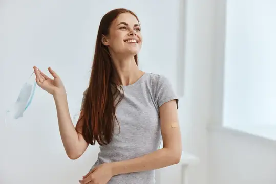 Улыбающаяся девушка снимает медицинскую маску после вакцинации
