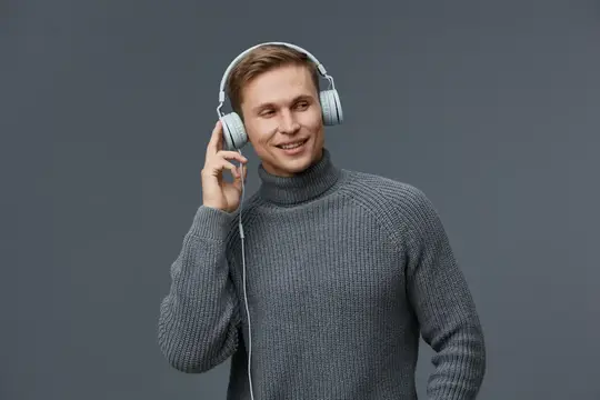 Улыбающийся парень в наушниках слушает музыку на сером фоне
