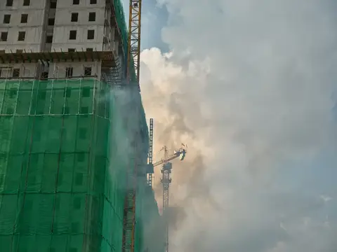 Строящееся высотное здание в зелёной сетке и башенный кран в дыму