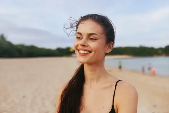 Улыбающаяся темноволосая девушка на песчаном пляже у воды