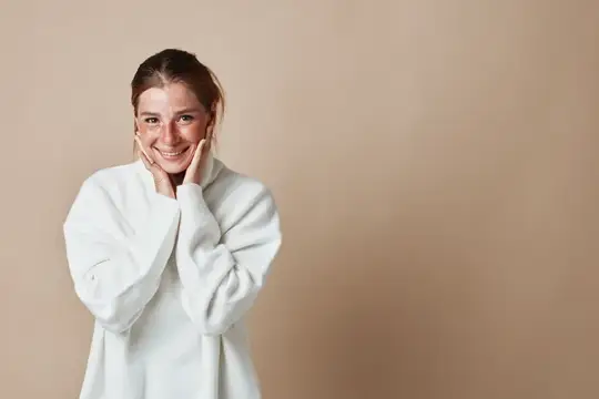 Улыбающаяся молодая женщина в белом свитере на бежевом фоне