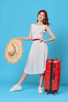 Улыбающаяся девушка в белом платье с соломенной шляпой и красным чемоданом