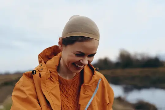 Улыбающаяся женщина в оранжевой куртке и шапочке на природе