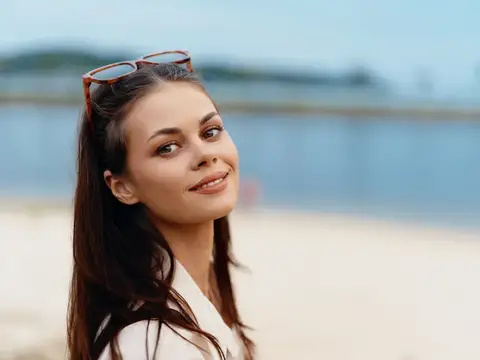 Улыбающаяся темноволосая девушка с очками на голове на пляже