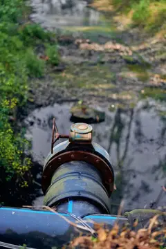 Труба и задвижка у дренажного выпуска, вода течет в загрязненный ручей