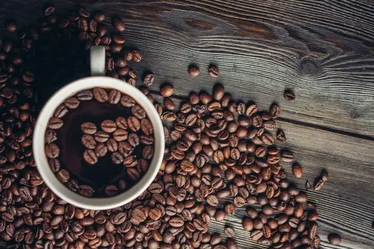 Чашка кофе и рассыпанные зерна на темном дереве