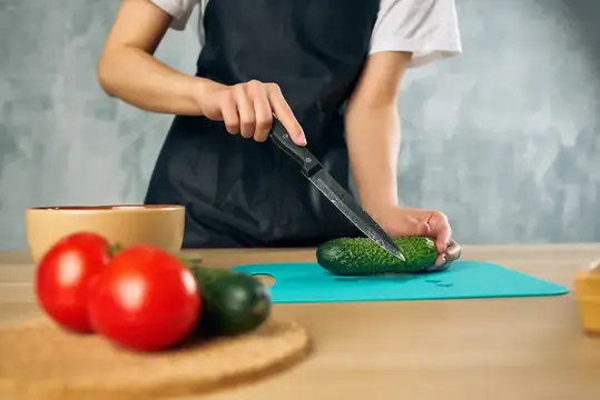 Женщина в черном фартуке на кухне нарезает овощи для салата, придерживаясь диеты