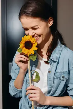 Улыбающаяся девушка с закрытыми глазами нюхает подсолнух