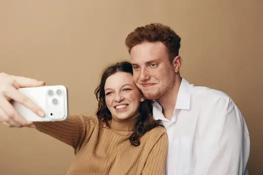 Улыбающаяся пара делает селфи на смартфон на бежевом фоне