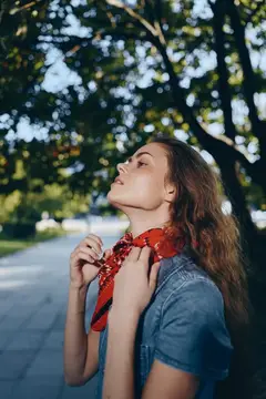 Молодая женщина с красным платком на шее в парке