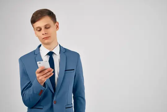 Молодой человек в синем костюме смотрит в смартфон