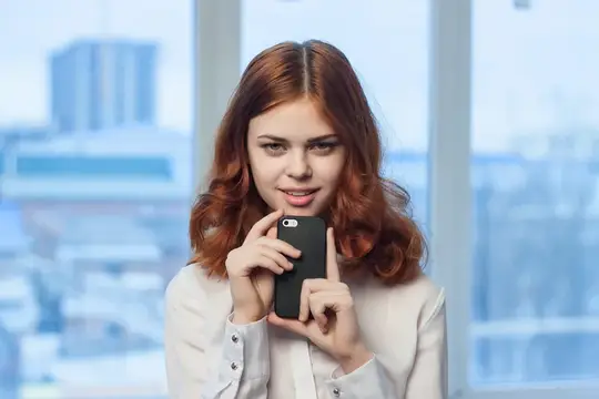 Рыжеволосая девушка с телефоном у окна с видом на город