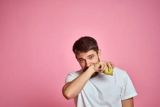 Молодой мужчина с яблоком в руке на розовом фоне
