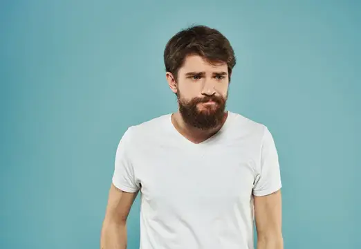 Задумчивый бородатый мужчина в белой футболке на голубом фоне