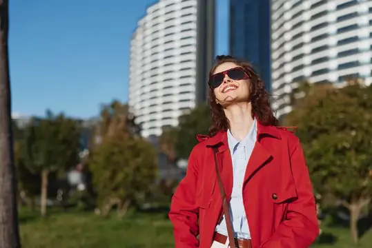 Улыбающаяся девушка в красном плаще и солнцезащитных очках на фоне высоток