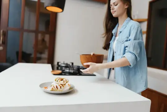 Молодая женщина готовит на светлой кухне с плитой