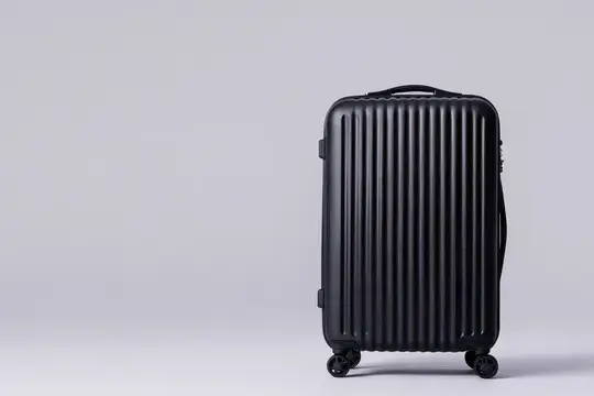 Черный пластиковый чемодан на колесиках стоит на сером фоне