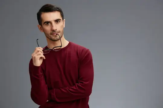 Задумчивый темноволосый мужчина с очками в руке на сером фоне