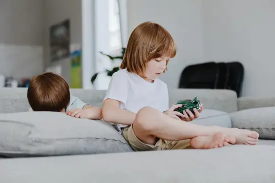 Рыжеволосый мальчик играет в портативную консоль на диване