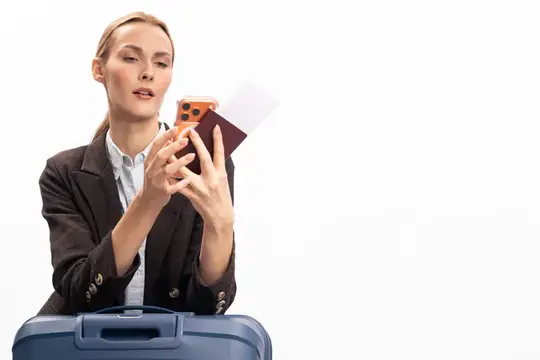 Девушка с паспортом и телефоном стоит за синим чемоданом