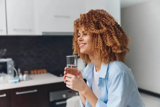 Улыбающаяся кудрявая девушка с стаканом воды на кухне