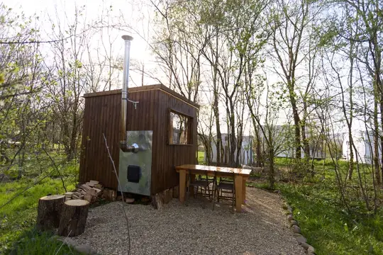 Деревянная баня с печной трубой и столом среди весенних деревьев