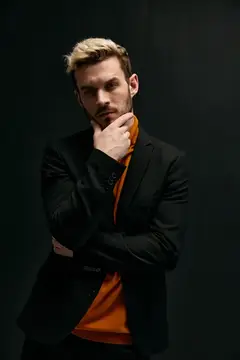 Задумчивый блондин в чёрном пиджаке на тёмном фоне