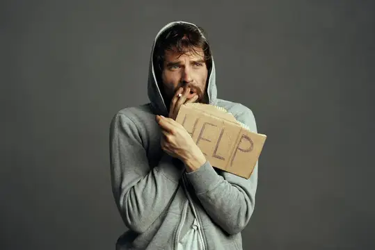 Бородатый мужчина в капюшоне с табличкой Help на сером фоне