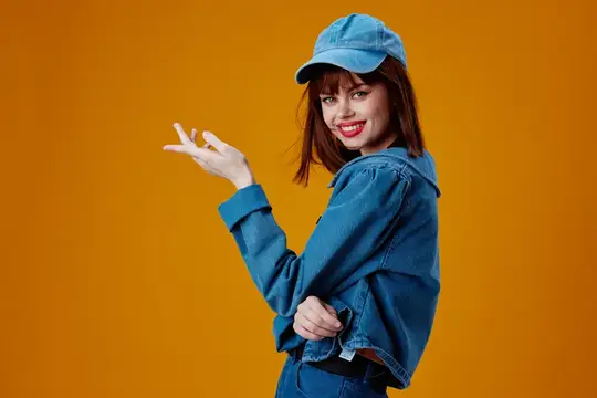 Улыбчивая девушка в джинсовой кепке и куртке на оранжевом фоне
