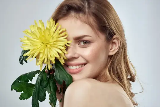 Улыбающаяся светловолосая девушка с жёлтой хризантемой у лица
