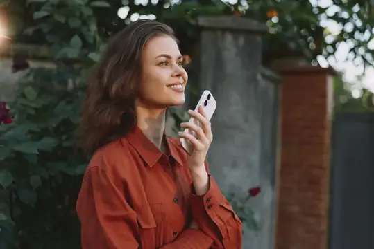 Улыбающаяся девушка в терракотовой рубашке слушает голосовое сообщение
