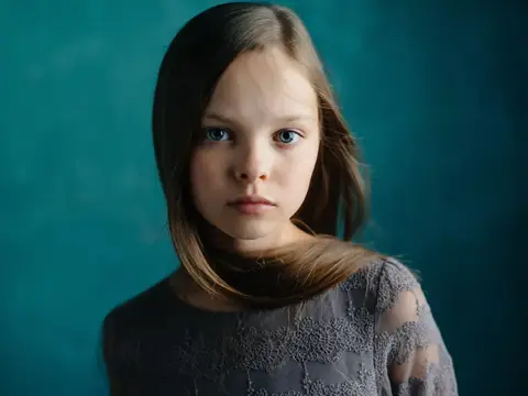 Светловолосая девочка с серьёзным взглядом на тёмно-бирюзовом фоне