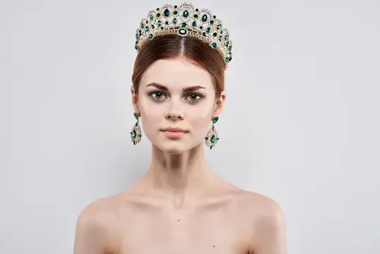 Молодая женщина в роскошной короне с изумрудами на светлом фоне