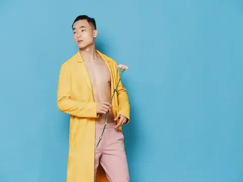 Азиатский мужчина в жёлтом пальто с цветком на голубом фоне