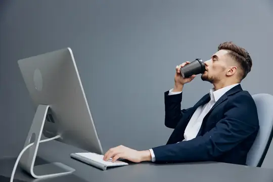Уставший менеджер с чашкой кофе работает перед компьютером в офисе