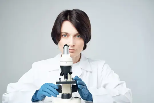 Молодая женщина-ученый в белом халате работает с микроскопом