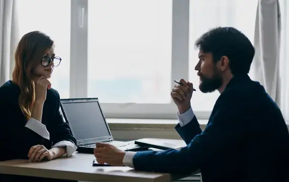 Бизнесмен в костюме и женщина общаются на работе, сидя друг напротив друга за столом в офисе