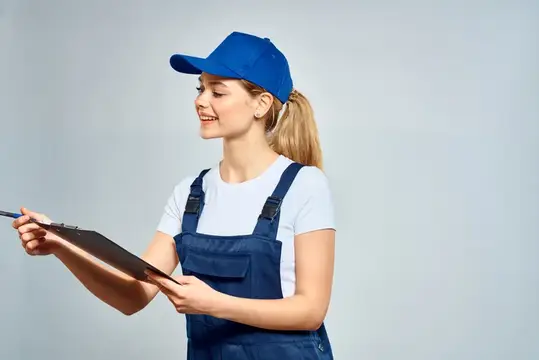 Улыбчивая девушка в синей кепке и комбинезоне с планшетом