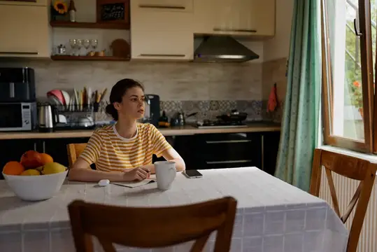 Молодая женщина в полосатой футболке сидит за столом на кухне