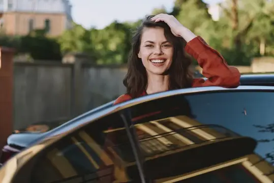 Улыбающаяся темноволосая женщина выглядывает из окна автомобиля