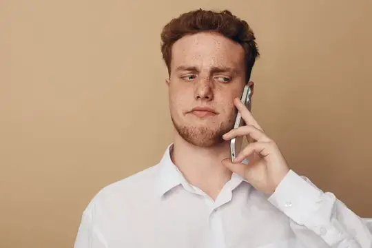 Подозрительный молодой человек в белой рубашке прижимает смартфон к уху, глядя в сторону с сомнением