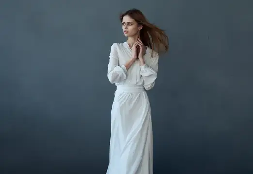 Молодая женщина в белом платье на сером фоне