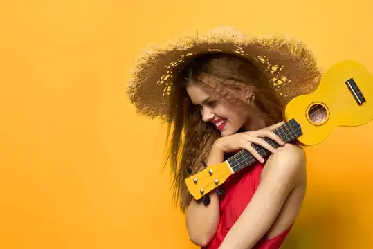 Улыбающаяся девушка в соломенной шляпе с желтой укулеле на оранжевом фоне