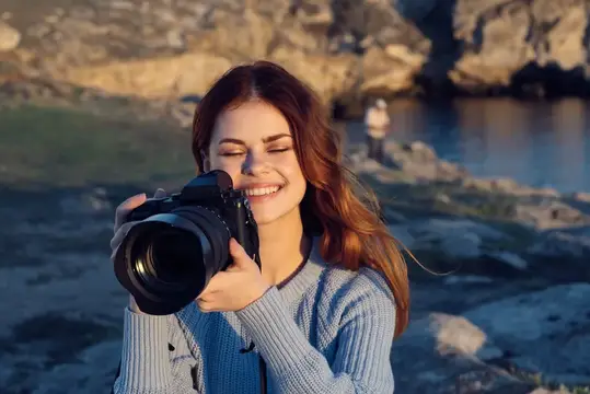 Улыбающаяся девушка с фотокамерой на скалистом берегу