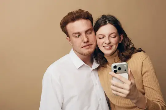 Улыбающаяся пара смотрит в смартфон на бежевом фоне