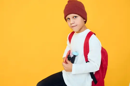 Мальчик в шапке с рюкзаком и пеналом на жёлтом фоне