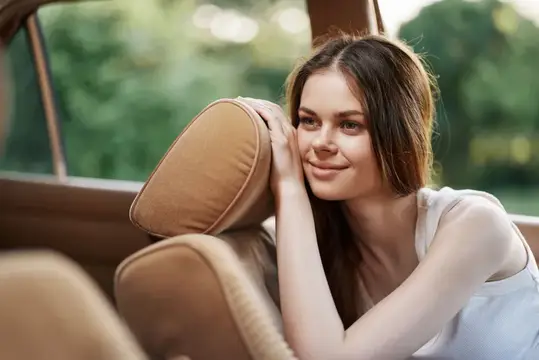 Молодая женщина с улыбкой прислонилась к подголовнику в салоне автомобиля