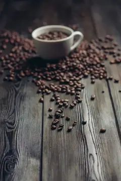 Белая чашка с кофейными зёрнами на тёмном деревянном столе