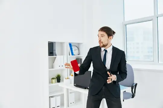 Удивлённый мужчина в костюме с красным смартфоном в офисе